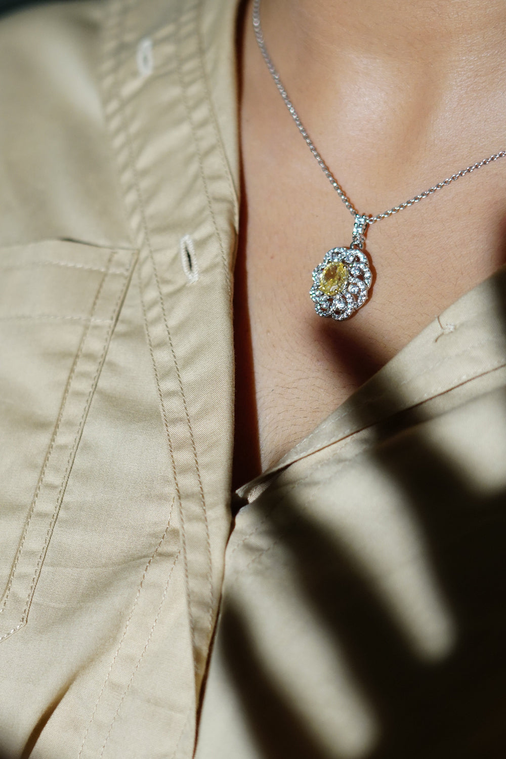 Necklace with a yellow gemstone pendant worn by a person in a beige shirt.